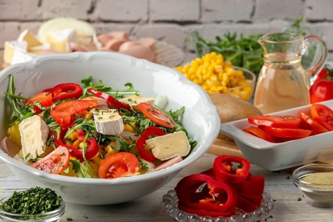 Fresh mixed salad of tomatoes, camembert, potatoes, sausage and arugula in a bright atmosphere
