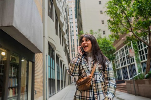 Young woman smiling and talking on her mobile phone while walking through a city alley lined with