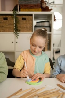 A young girl in a colorful shirt focuses on a creative art project, using modeling clay and a
