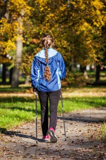 Nordic walking adventure and exercising concept, woman hiking withnordic walking poles in park