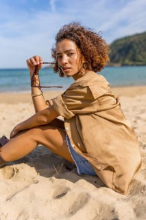 Vertical side view of a beauty Arab beauty model sitting on sandy beach taking off the sunglasses
