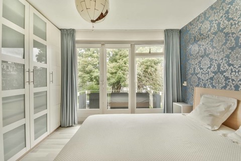 Spacious bedroom featuring elegant patterned wallpaper, a comfortable bed, and glass doors opening