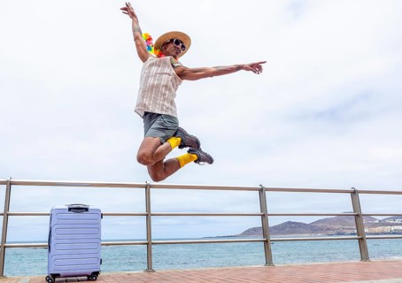 A joyful LGBTQIA+ man, with a suitcase, leaps in the air, excitedly preparing for travel and