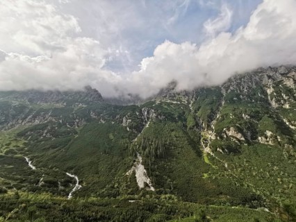 Wide view of lush mountain landscape with green valleys and dramatic clouds covering the peaks,