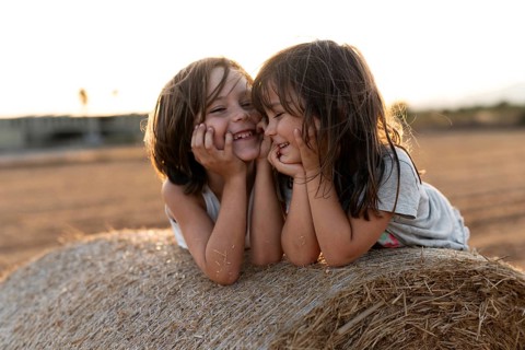 Two children with bright smiles lie on a bale of hay in a sunlit field, embodying the joy and
