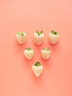White strawberries arranged in a row forming a triangle on a pink background. top view with copy