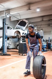 Young mechanic lifting a car tire in a professional workshop, demonstrating expertise and