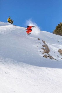A snowboarder in red gear performs a daring jump on a snow covered mountain slope under a clear
