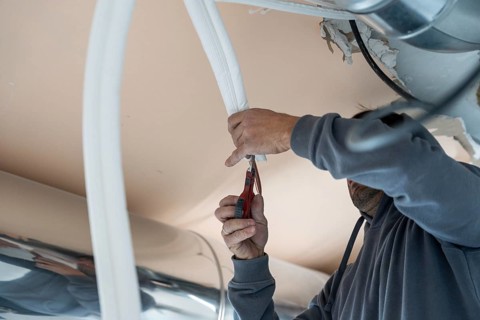 Hvac technician cutting insulation for an air conditioning duct, carefully trimming material for a