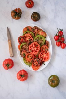 A colorful assortment of sliced heirloom tomatoes garnished with fresh herbs, arranged on a white