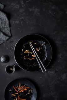 Overhead black empty bowl with pair of chopsticks and leftovers of Korean cuisine Japchae at table