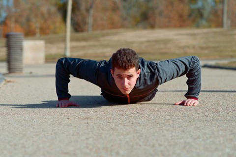 A young athlete performs push ups on a sunny day outdoors, exhibiting strength and focus. He is