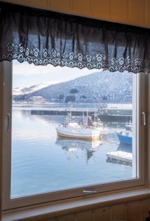 A serene winter scene in Botnhamn, Norway, viewed through a lace-trimmed window, framing fishing