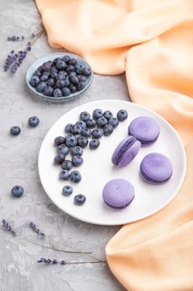 Purple macarons or macaroons cakes with blueberries on white ceramic plate on a gray concrete