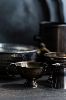 A collection of vintage metal cups with textured handles is displayed on a dark surface. The dim