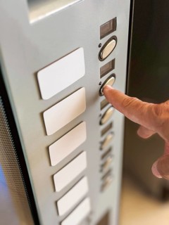 A close-up view of a person's hand pressing a button on an elevator panel. The panel features