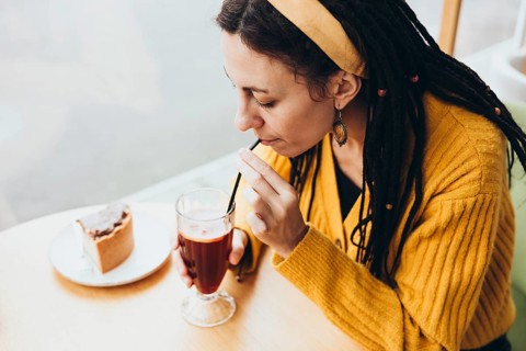 A woman with dreadlocks in a cafe sips a beverage through a straw Wearing a yellow sweater and