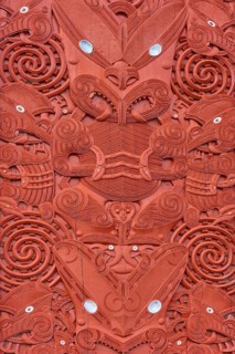 Close-up of a symmetrical Maori wood carving with red decorations, New Zealand Maori Arts and
