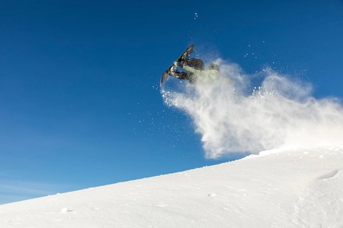 A snowboarder performs an impressive air trick, lifting off the fresh powder in a remote mountain
