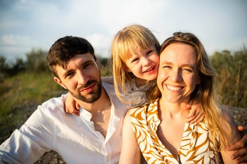 A joyful family of three enjoys a sunny day at a beach in Italy. The scene captures the happiness