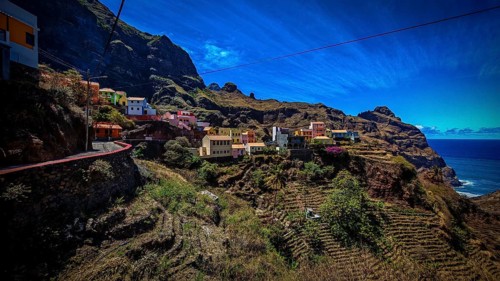 Panoramic view, small settlement, colorful village, nestled in raw, dramatic mountains under blue