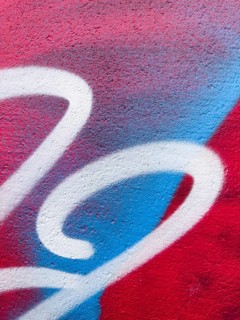 A close-up of vibrant graffiti artwork, showcasing red, blue, and white colors on a textured wall.
