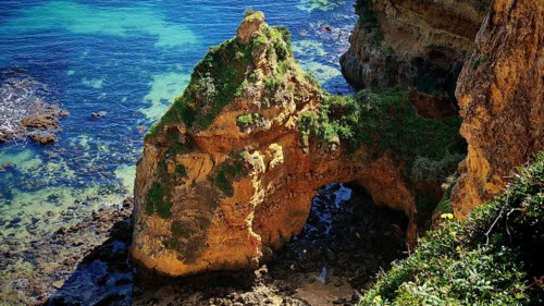 Cliffs and remarkable rock arch on a sun-drenched coast with clear sea, Praia Dona Ana, Lagos,