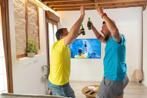 Friends reacting with excitement after a goal while watching a match on television. Spontaneous