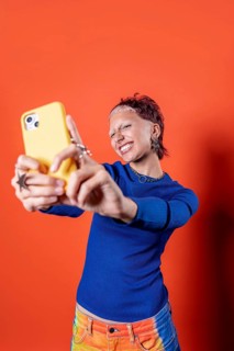 Fashionable woman in colorful trousers, tooth gems and blue sweater takes a selfie against a