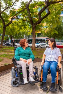 Two multi-ethnic disabled female friends in wheelchair talking in a city park