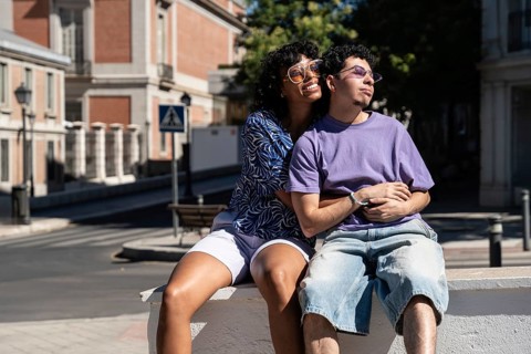 A joyful, multiethnic LGBTQ+ couple shares a tender moment while seated outdoors. The scene