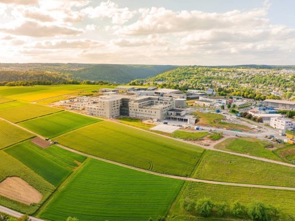 Large building surrounded by extensive green fields, embedded in a hilly landscape, construction of