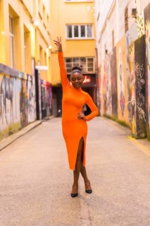 Fashionable urban style with a black African girl in an orange dress and black heels on a city