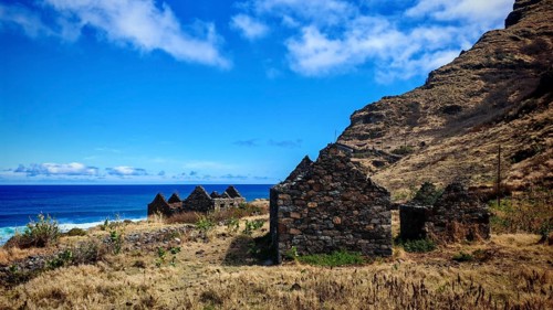 Dilapidated stone houses, volcanic stone ruins near the coast overlooking the blue sea, hiking,