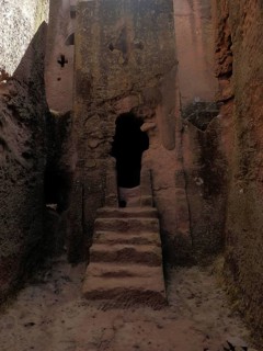 Entrance to a rock church with sandstone-colored steps and rough stone structure, UNESCO World