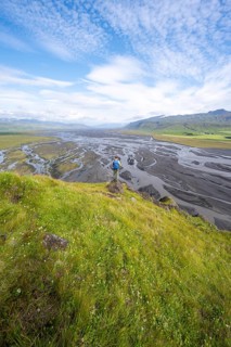 Hiker, young man on a hill, view over alluvial land, meandering river, Dímonarhellir, Suðurland,