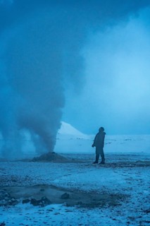 A man stands next to one of the steaming fumaroles at Hverir or Namafjall geothermal park in