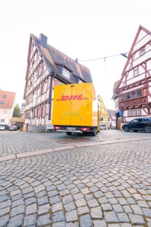 DHL delivery van on cobbled street in front of traditional half-timbered houses, urban environment,