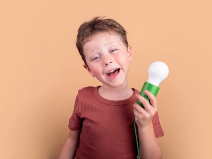 Cheerful young boy holding a white bulb, wearing a rust colored shirt. He stands against a peach