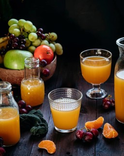 Assorted glasses and bottles of fresh orange juice surrounded by vibrant fruits, including grapes