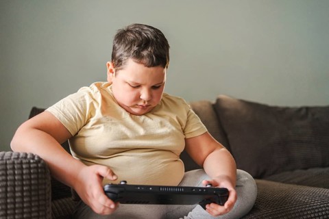 Young boy focused on playing a hand held gaming console while sitting comfortably on a cushioned