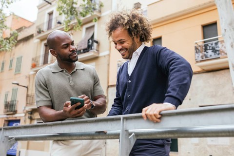 Two men enjoying a break outside a coworking space share a smartphone, engaged in a friendly and