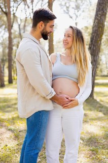 A pregnant woman stands outside with her partner, sharing a joyful moment. They embrace under the