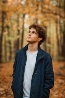 Young man standing in a Quebec forest during autumn, surrounded by colorful leaves. He wears a
