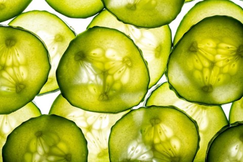 A close up image showcasing thin, translucent cucumber slices against a white background. The