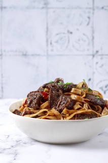 Udon noodles with Mongolian beef, green onions and vegetables, in a white plate, on a light