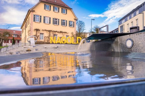 A well with running water next to the Nagold logo in front of an old building, Nagold, Calw