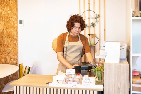 A organic products skin care shop cashier wearing a brown apron works diligently at the counter,