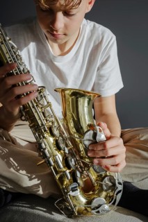 A young musician concentrates while holding a saxophone, captured in natural light. The focus on