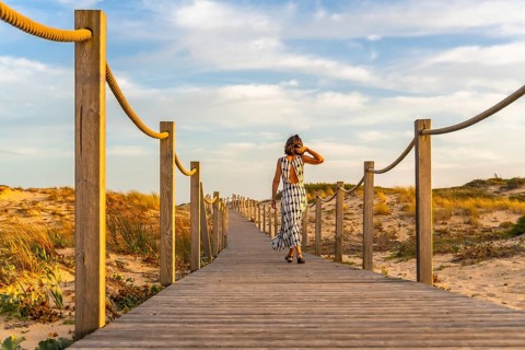 Woman in a dress enjoying a leisurely walk along a wooden boardwalk, leading through sand dunes to